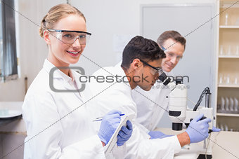 Smiling scientist looking at camera while colleagues working with microscope