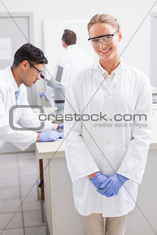 Smiling scientist looking at camera while colleagues working behind