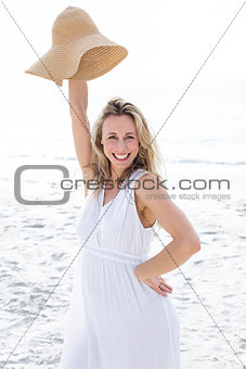 Smiling blonde in white dress looking at camera and holding straw hat