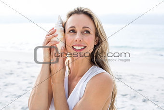 Smiling blonde in white dress listening the seashell