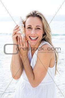 Smiling blonde in white dress listening the seashell