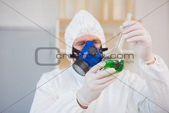 Scientist in protective suit examining green precipitate