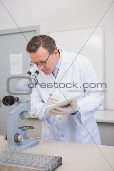 Scientist analysing microscope writing on clipboard