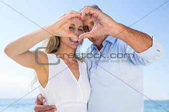 Happy couple smiling at camera and doing heart shape with their hands