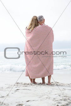 Happy couple hugging each other and looking at the sea with blanket around them