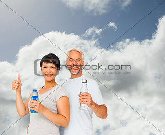 Composite image of fit couple with water bottles gesturing thumbs up