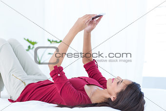 Beautiful woman using her smartphone lying on bed