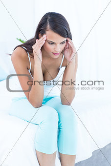 Pretty brunette sitting on bed suffering from head ache