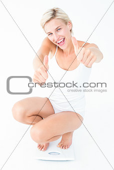 Happy blonde woman crouching on a scales with thumbs up