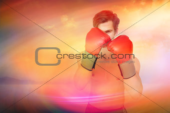 Composite image of muscly man wearing red boxing gloves in guard position