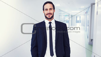 Composite image of smiling businessman in suit standing with hands in pockets