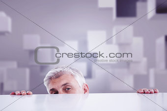 Composite image of businessman peeking over desk