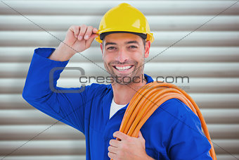 Composite image of confident repairman wearing hard hat while holding wire roll