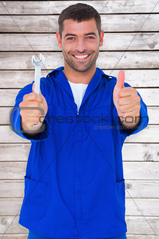 Composite image of smiling mechanic holding spanner while gesturing thumbs up