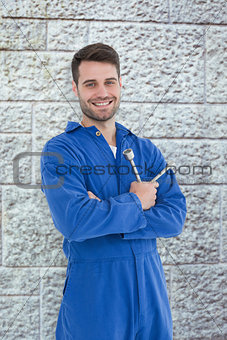 Composite image of smiling young male mechanic holding spanner