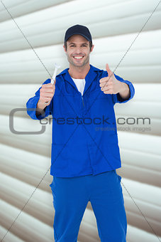 Composite image of happy mechanic holding spanner