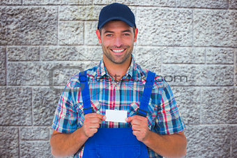 Composite image of portrait of happy handyman holding visiting card