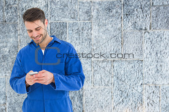 Composite image of male mechanic text messaging through mobile phone