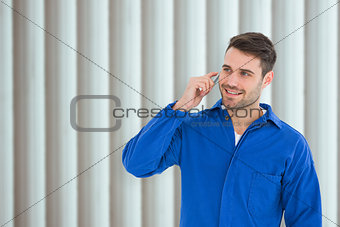 Composite image of happy young male mechanic using mobile phone
