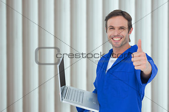 Composite image of mechanic holding laptop while showing thumbs up
