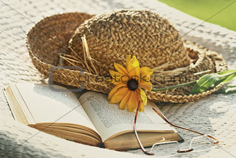 Close up of straw hat, sunglasses and book on a hammock