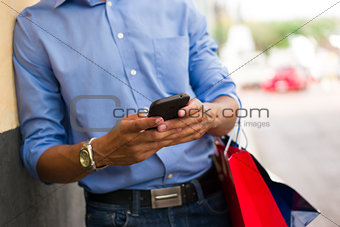 African American Man Typing Message On Phone Shopping Bags