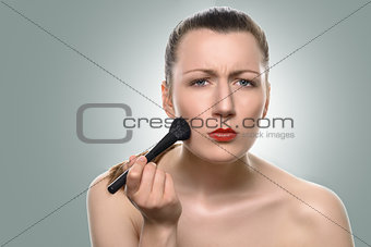 Young woman applying blush on her cheeks