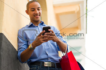 African American Man Text Messaging On Phone With Shopping Bags