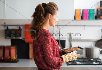 Woman in profile standing in kitchen holding hot loaf tin