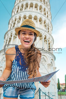 Smiling woman tourist holding map in front of Tower of Pisa