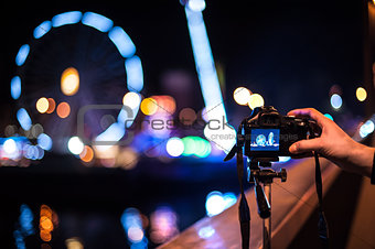 A hand holding a camera on a tripod in front of a black background with spotlights