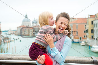 Laughing mother holding daughter who is whispering in her ear
