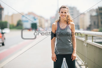 Smiling woman jogger standing still on bridge