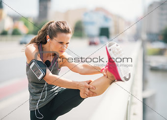 Woman runner stretching leg on rail in summer in urban setting