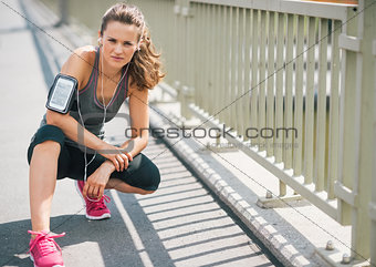 Woman runner kneeling on sidewalk in summer in urban setting