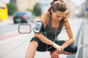 Woman runner kneeling, looking down, listening to music