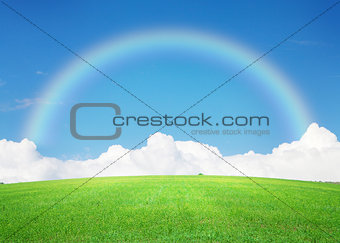 Green grass field, blue sky with clouds on horizon and rainbow