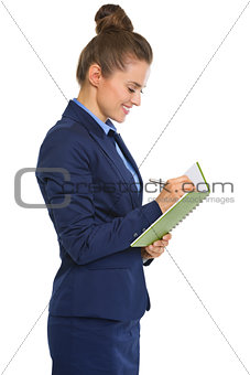 Smiling businesswoman in profile standing, writing in notebook