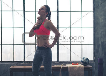 Fit woman in profile wiping sweat off neck in loft gym