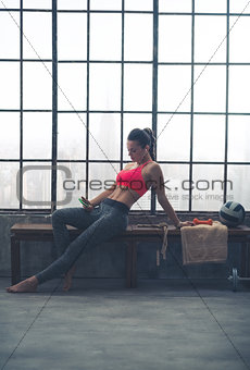 Woman reclining on bench selecting music in loft gym