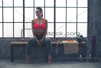Fit woman sitting on bench in workout gear listening to music