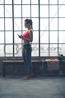 Fit woman selecting music on device in loft gym