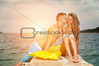 Young happy couple kiss on a beach during sunset
