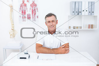 Smiling doctor looking at camera at his desk