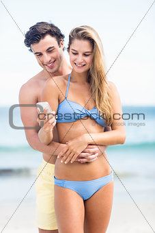 Happy couple in swimsuit looking at mobile phone