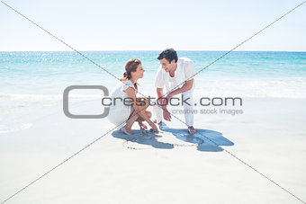 Happy couple drawing heart shape in the sand