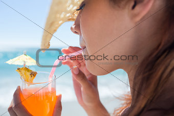 Brunette wearing straw hat and drinking a cocktail