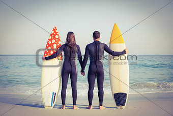 Couple in wetsuits with surfboard on a sunny day