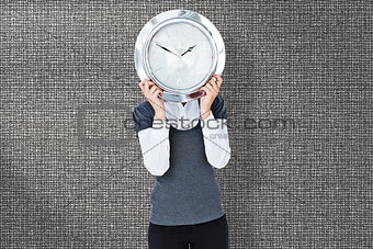 Composite image of woman holding clock in front of her head