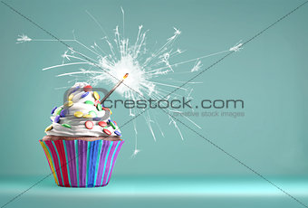 Delicious cupcake with a glittering sparkler and smarties on a whipped cream. Colored disks background.